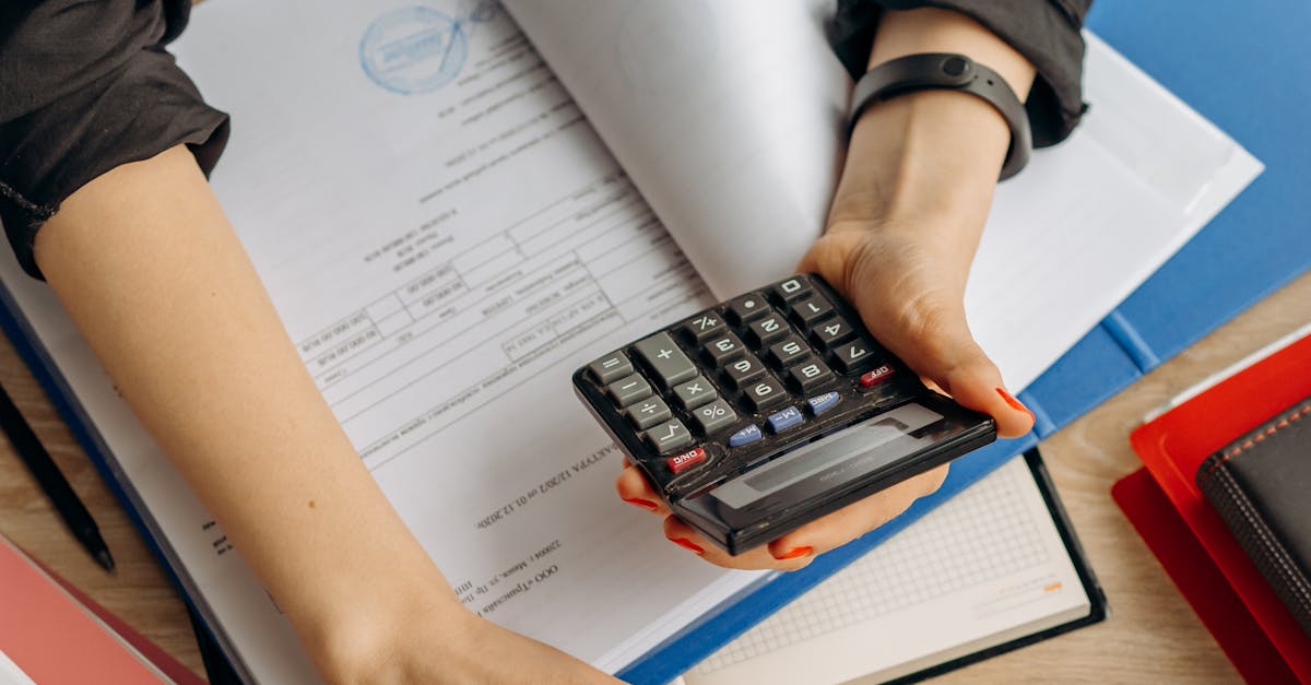 A business professional uses a calculator among documents and laptop on a desk for financial tasks.